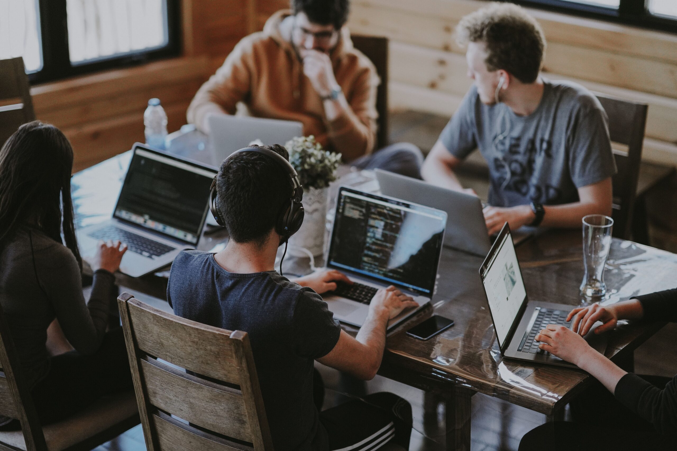 A group of coworking community members working together on laptops around a wooden table.