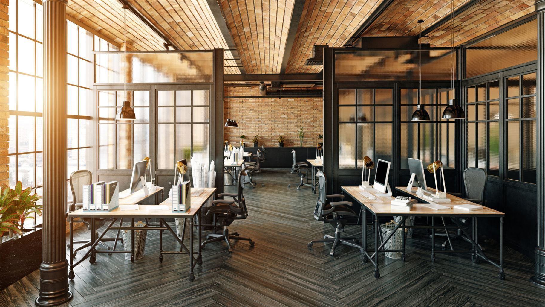 A modern industrial-style office with exposed brick walls, large windows, and wooden desks with computers and office supplies.