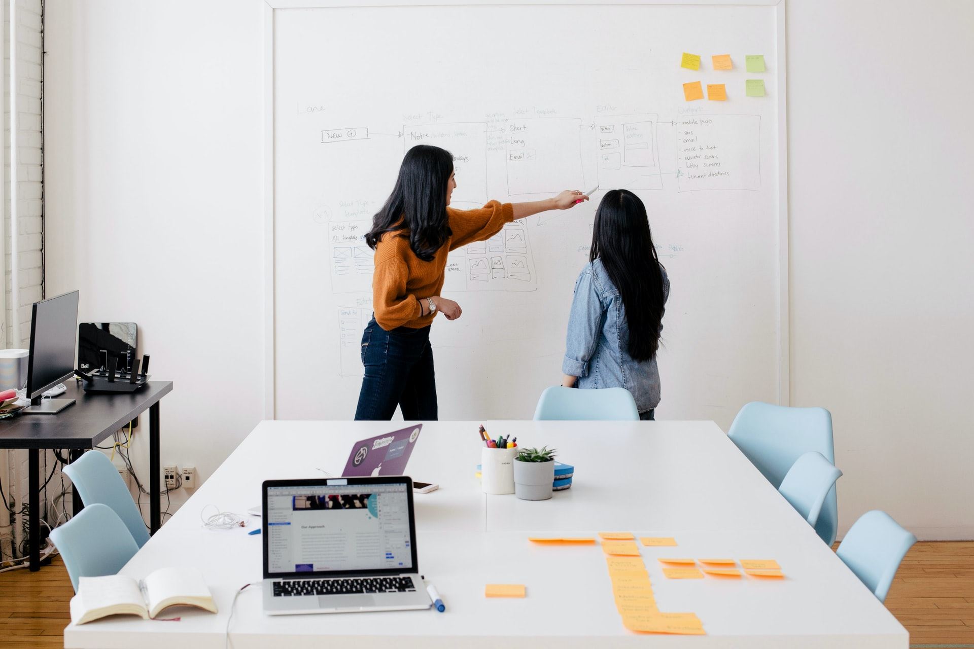 Two women pointing to a whiteboard in a conference room.