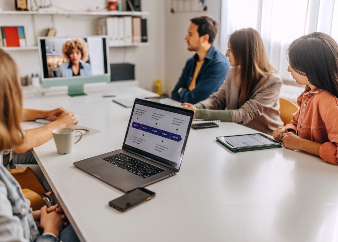 A group of people in a meeting room having a video conference with a colleague on a screen.