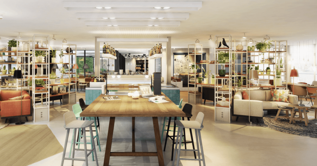 A bright and cozy coworking space with a large wooden table, colorful chairs, lounge areas, and lots of plants.