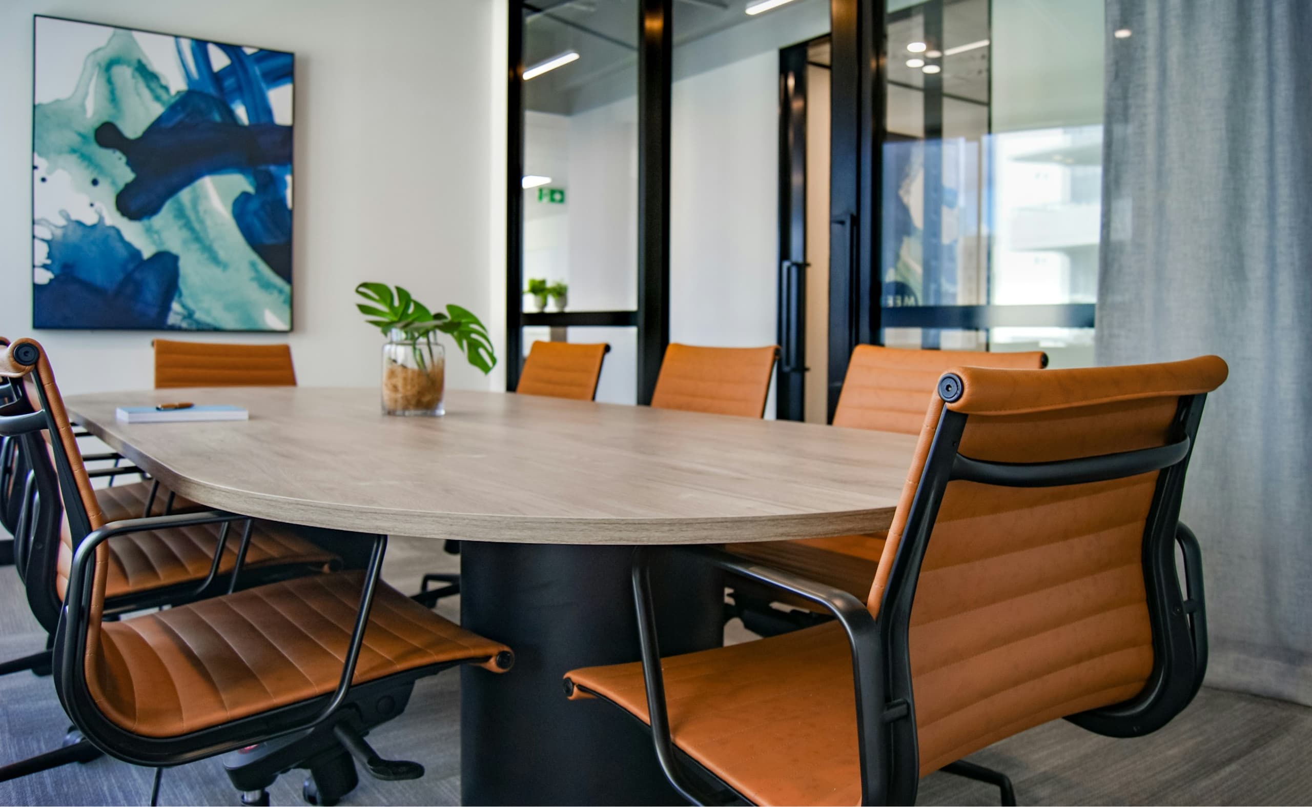 Bright meeting room with tan leather chairs and a plant centerpiece on the table.