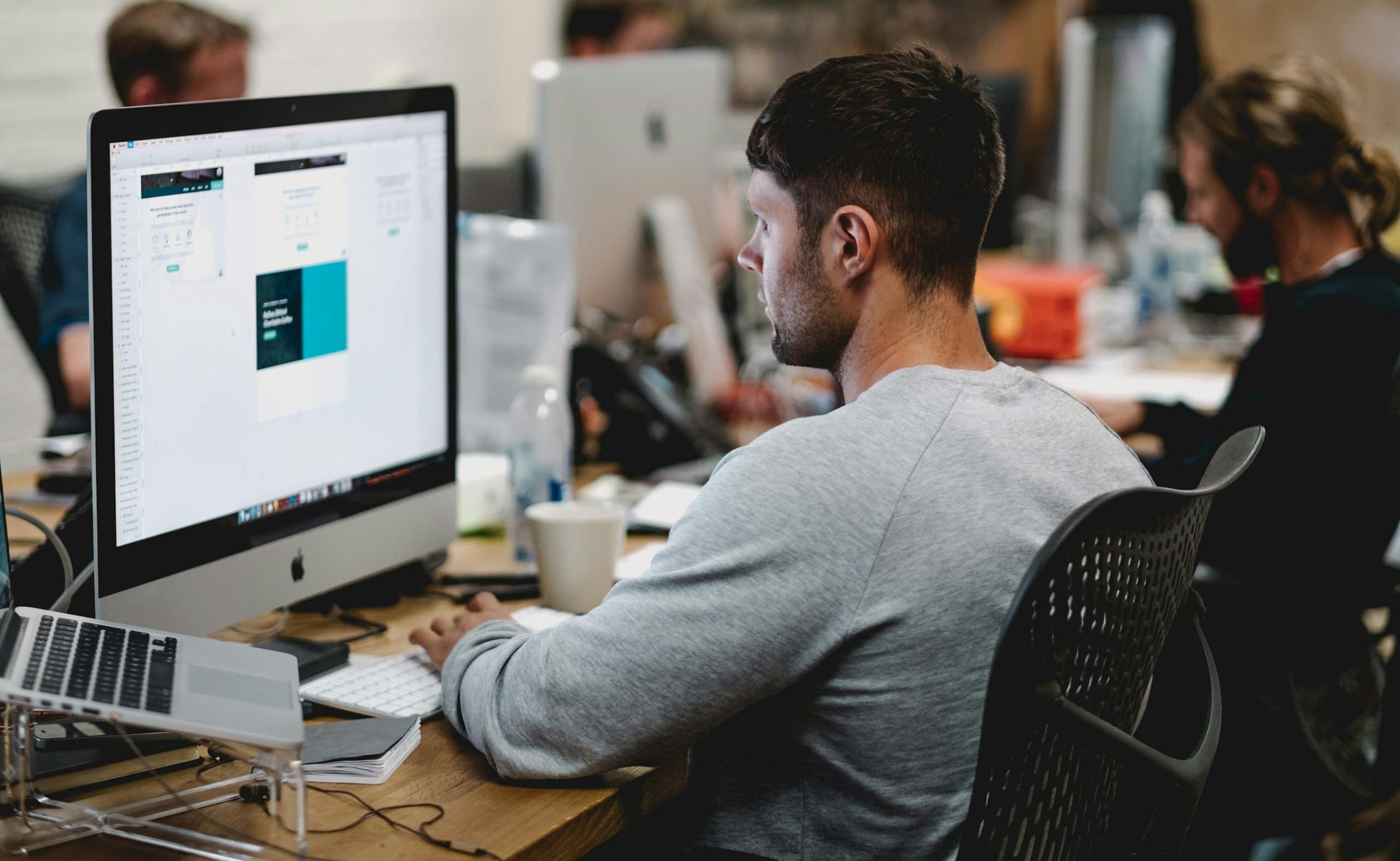 Man focused on his computer in a busy open-plan office environment.