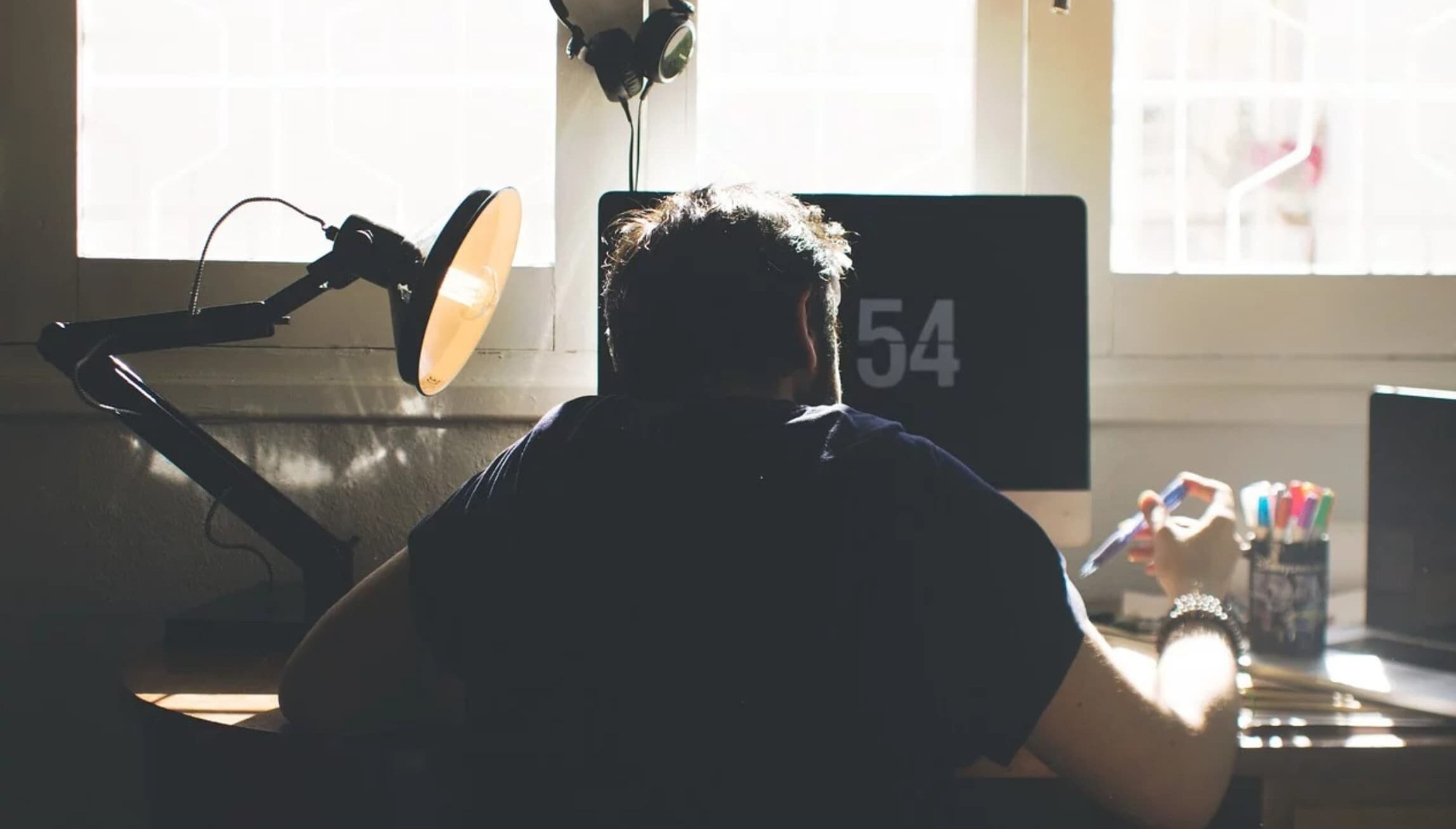 A person working at a desk in front of a computer, with sunlight coming through the window behind them.