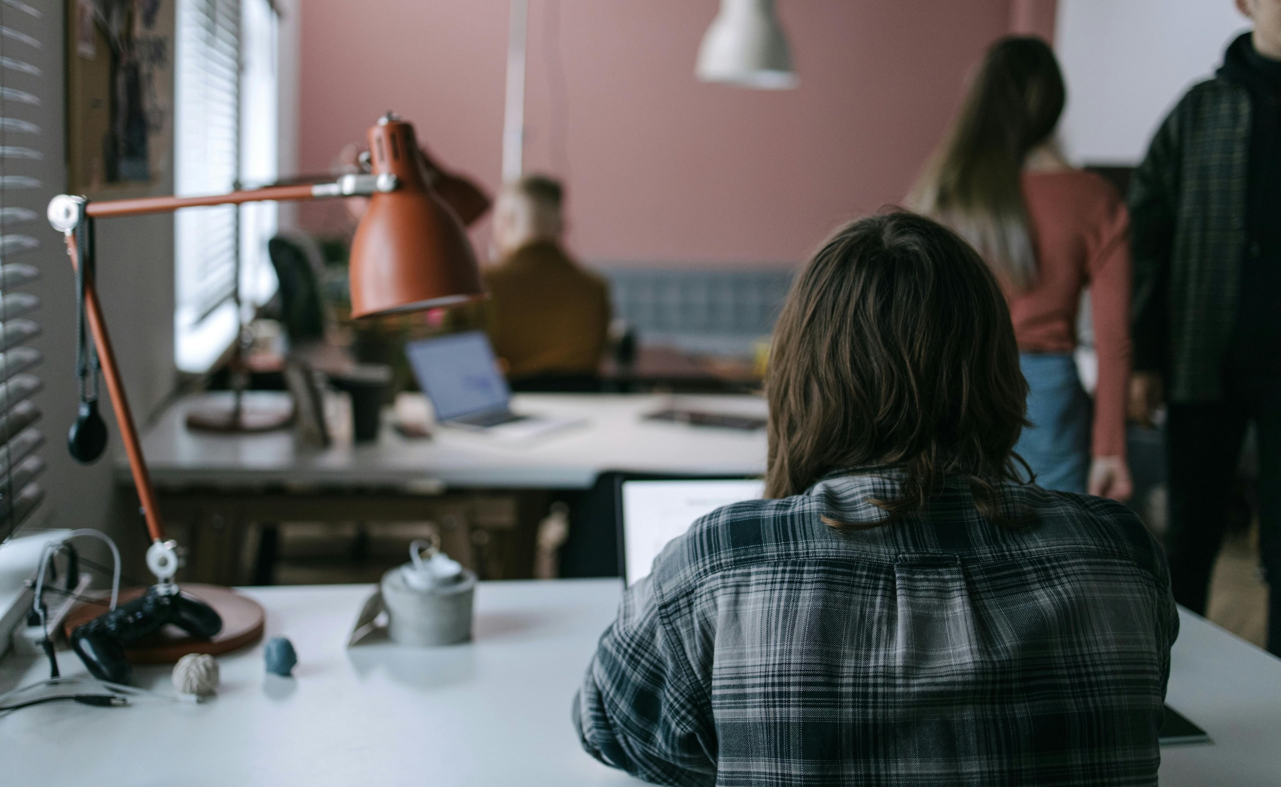 Person working at a desk in a shared office, with other people collaborating in the background.