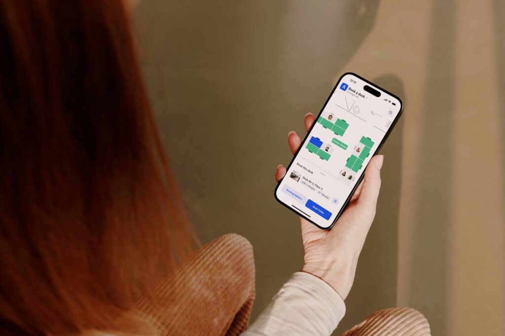 A person holds a phone displaying the Archie app for booking a desk in a floor plan view.