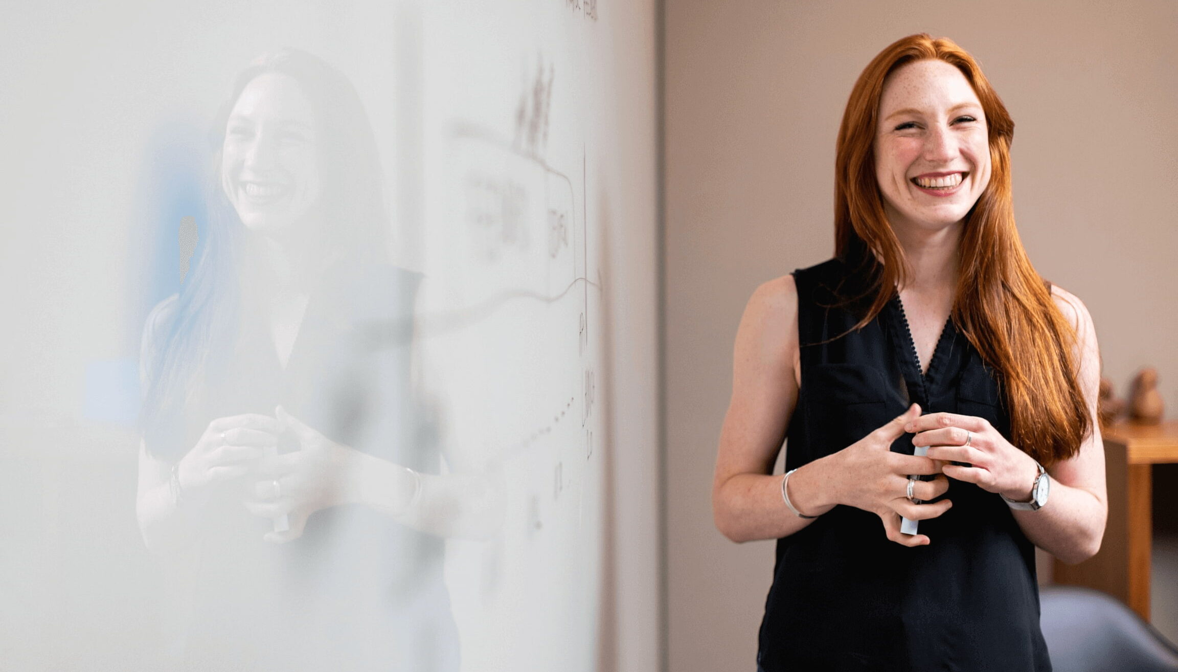Smiling woman standing next to a whiteboard during a presentation or team meeting in a modern office.