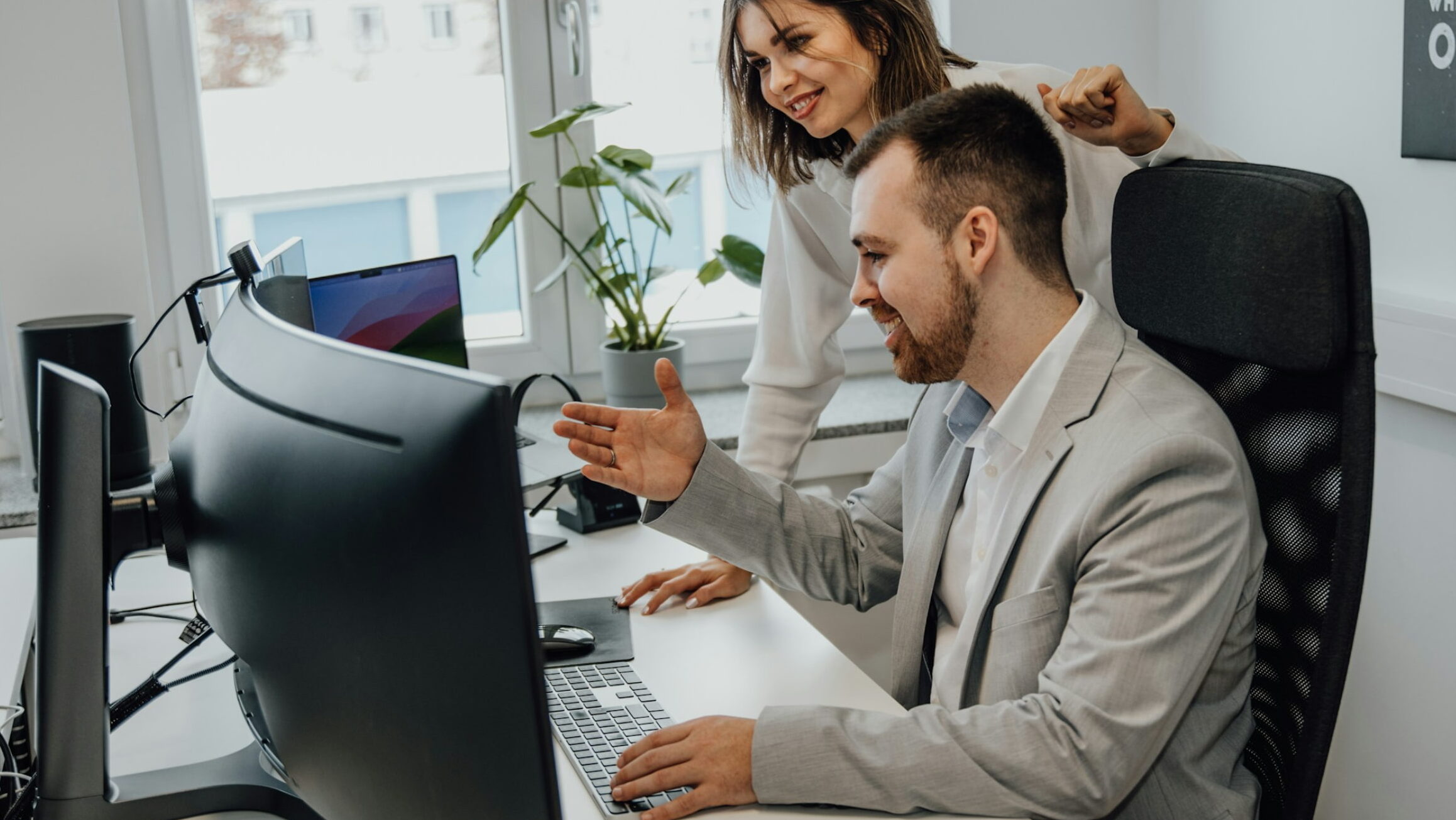 Two coworkers smiling and discussing something during an employee onboarding on a computer screen in a bright modern office.