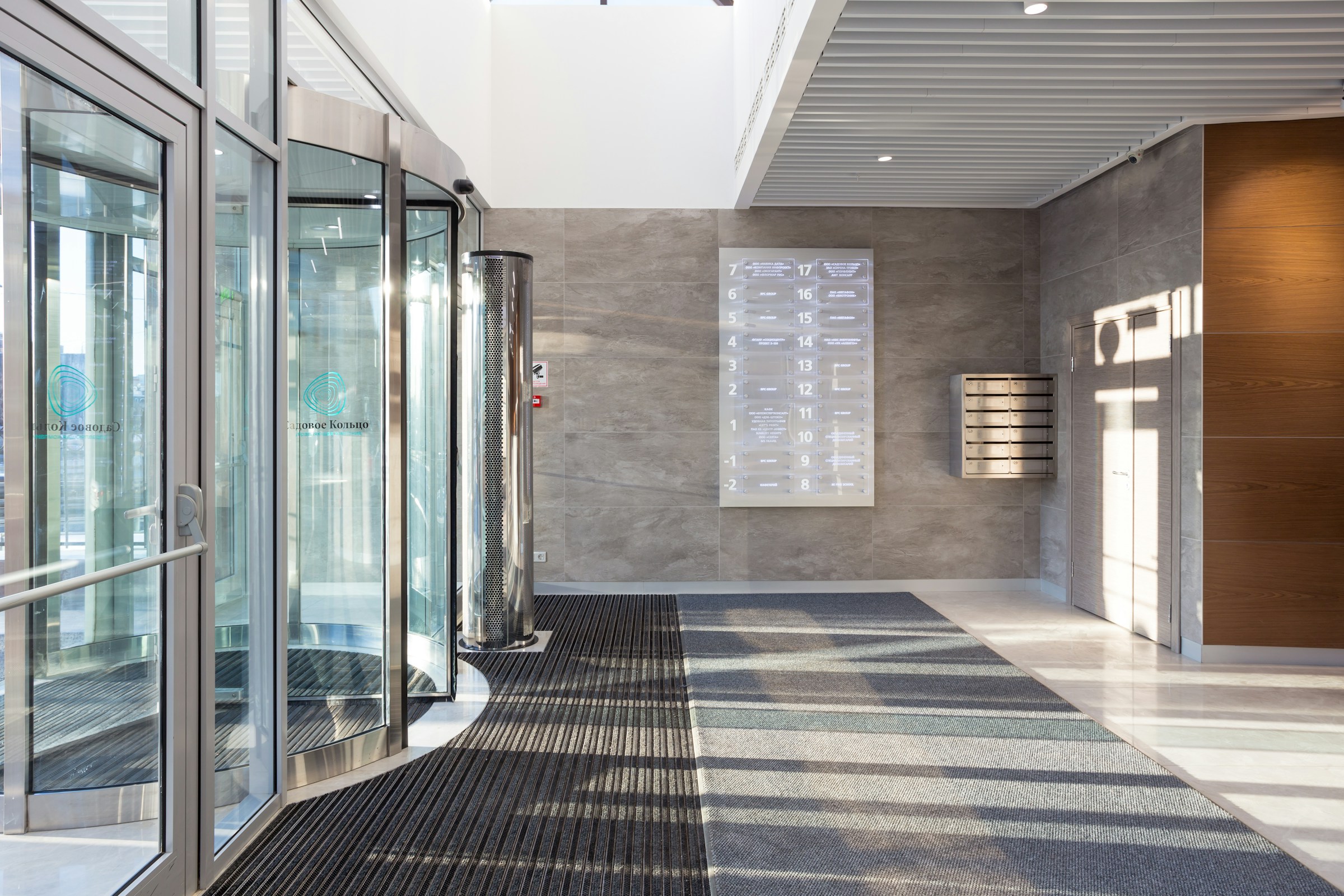 Bright office lobby with glass revolving doors, wall-mounted directory, and mailboxes.