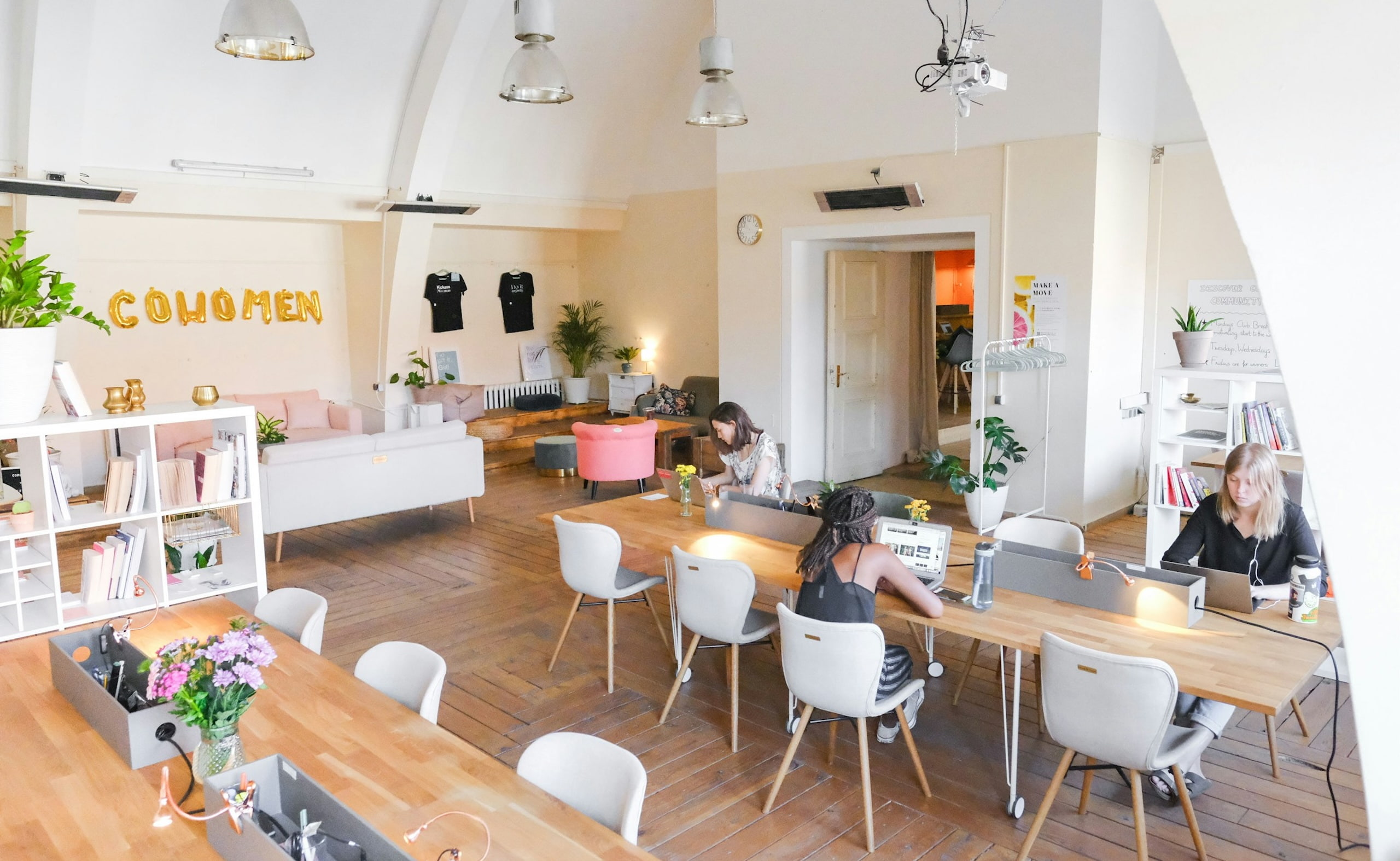 Bright coworking space with women working at shared wooden desks and cozy sofas.