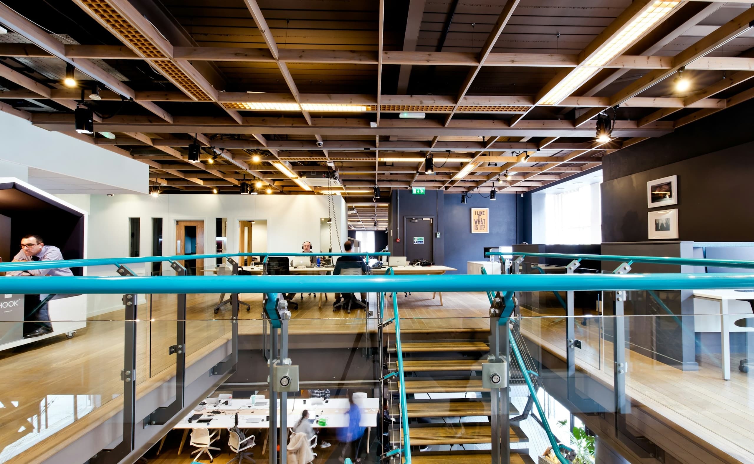 Spacious coworking area with desks on two levels, connected by stairs with blue handrails.
