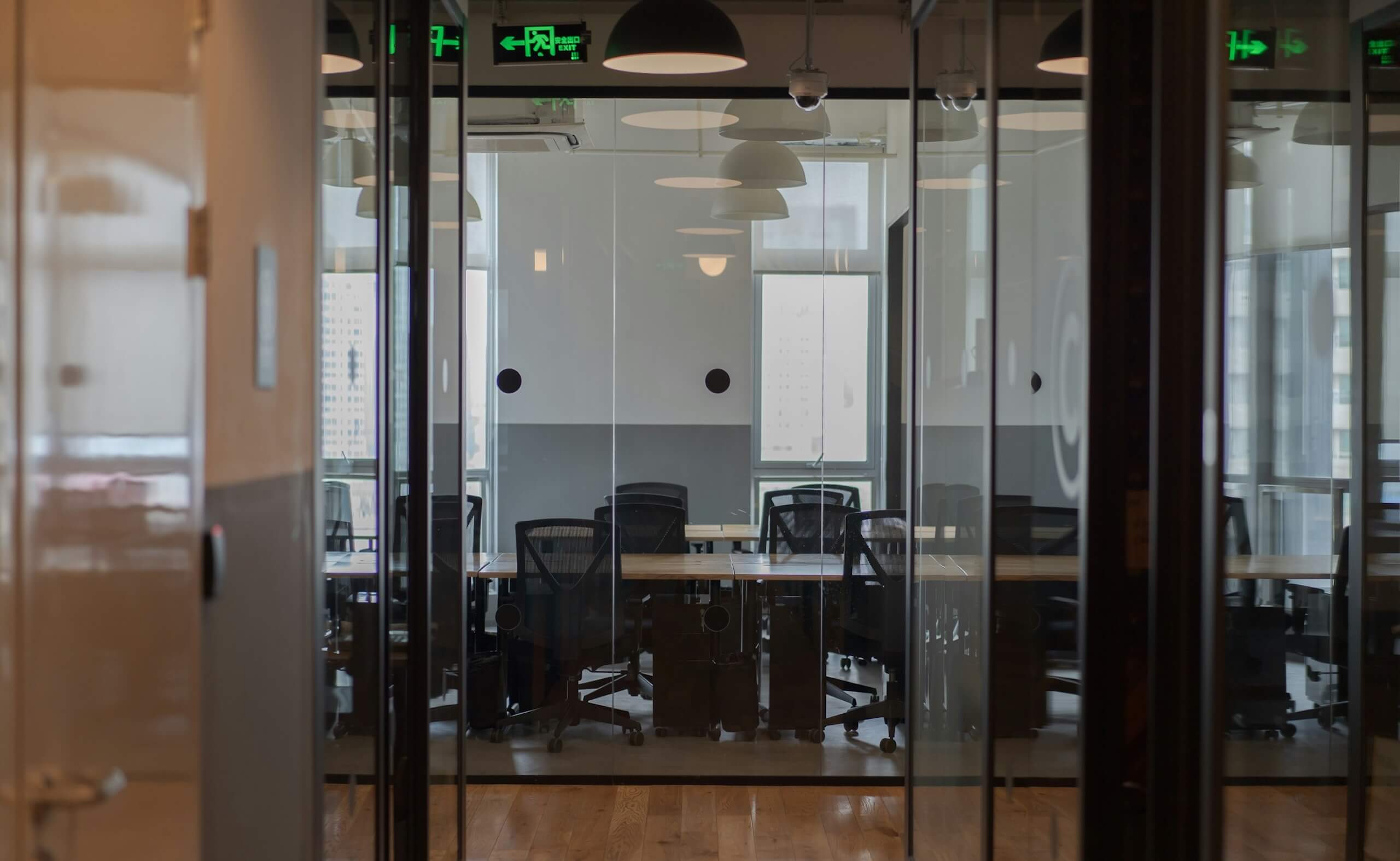 Glass meeting room inside a modern office with shared desks and chairs visible through the glass walls.