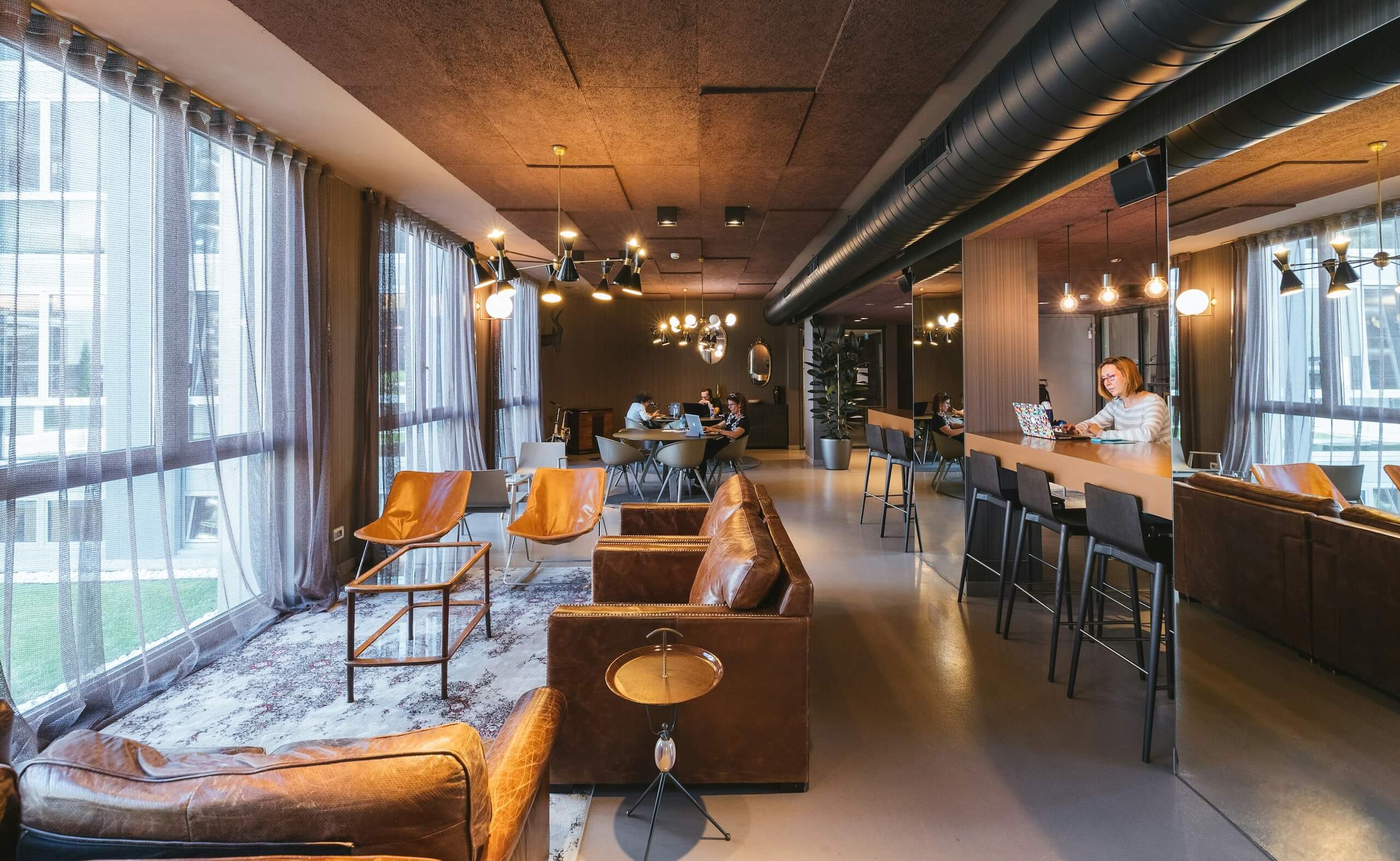 Modern coworking space with lounge seating, shared tables, and people working on laptops.